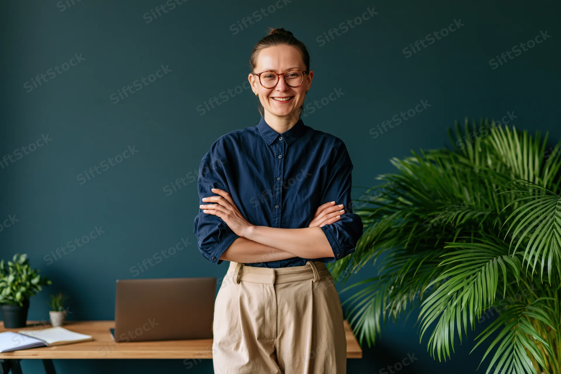 Young woman standing with arms crossed in front of a wooden desk in an office space