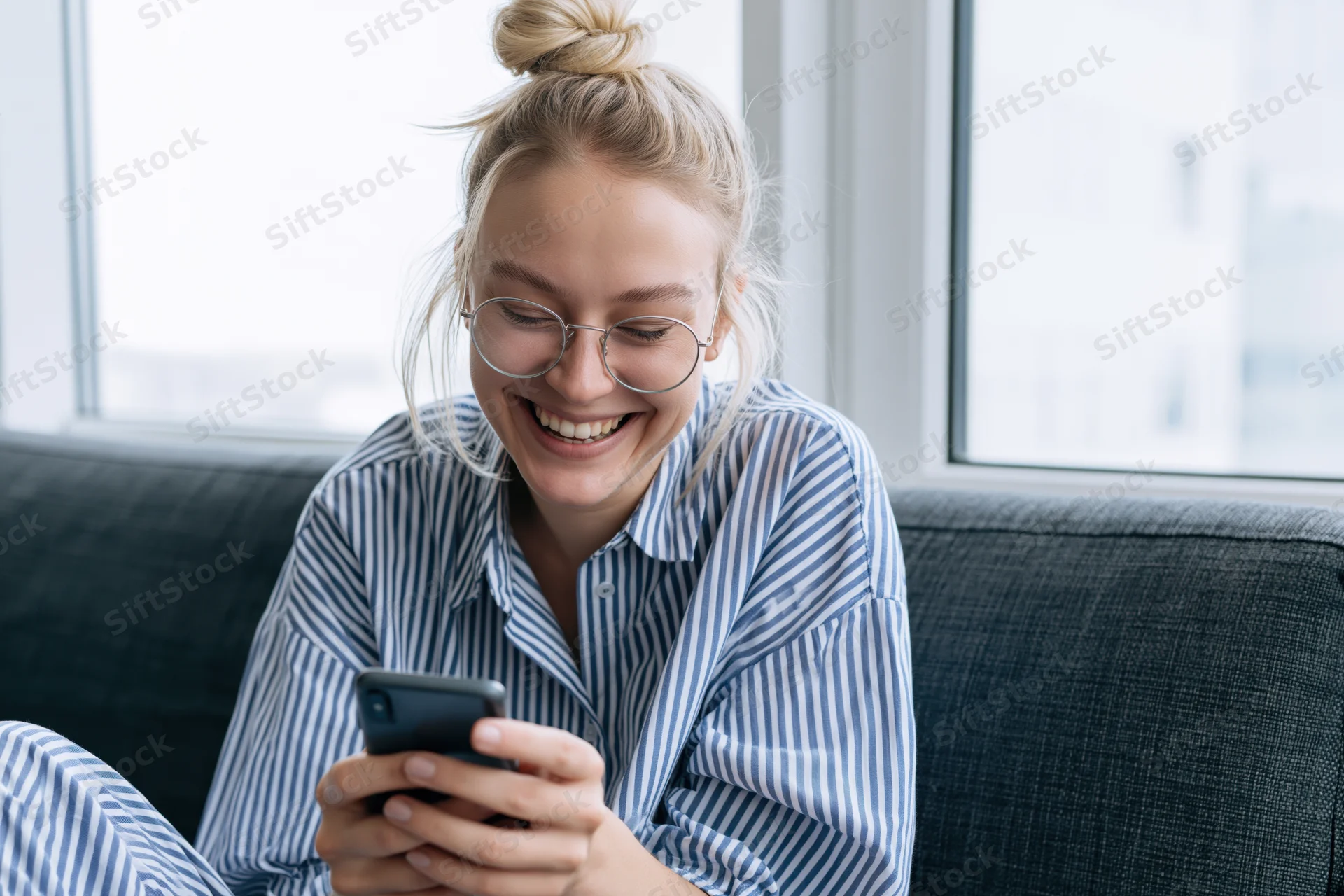 Young woman laughing while using smartphone on couch at home