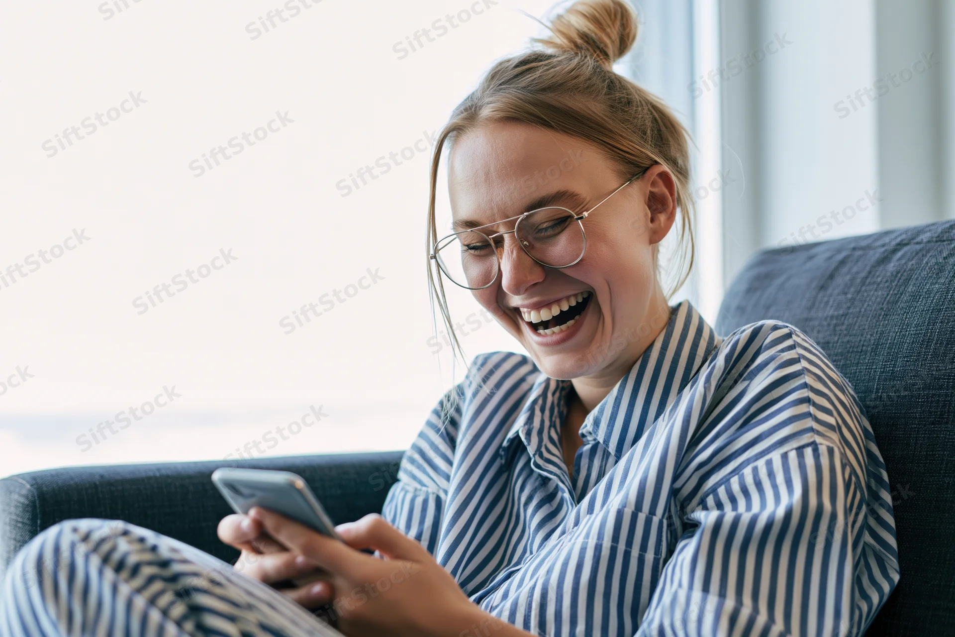 Young woman laughing while using smartphone on couch at home