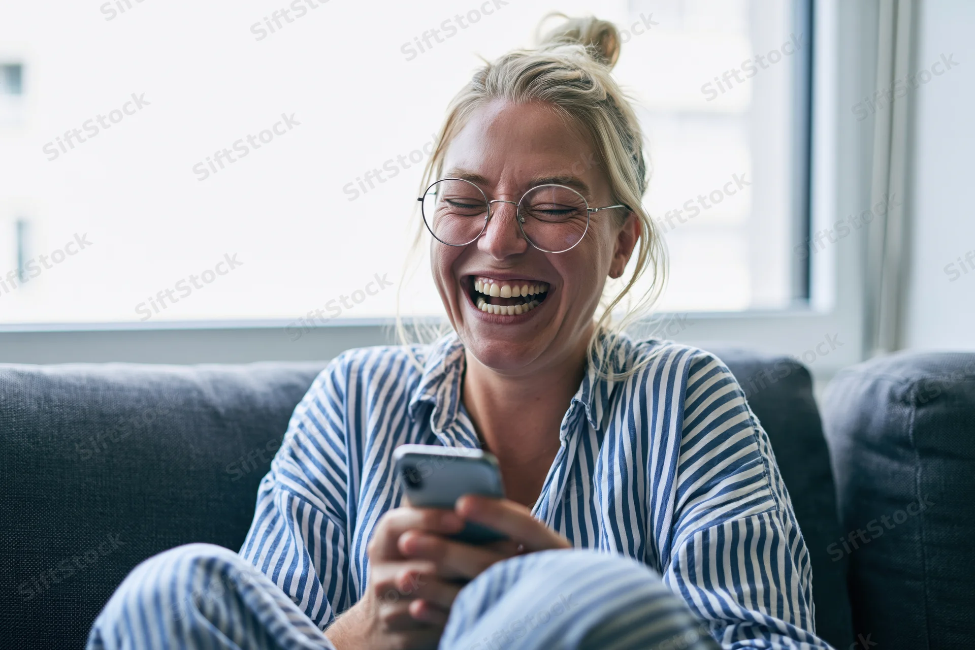 Woman laughing while using smartphone on couch at home