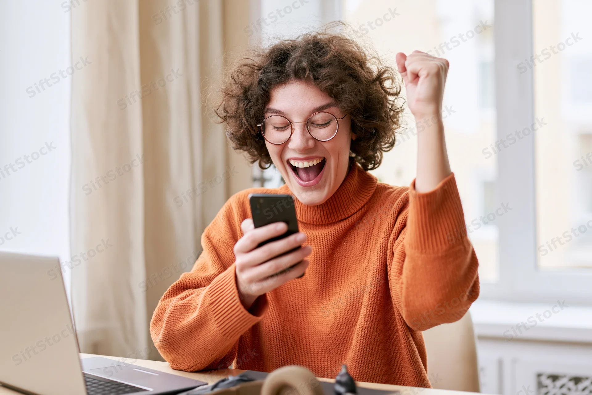 Woman celebrating good news on smartphone at home office desk