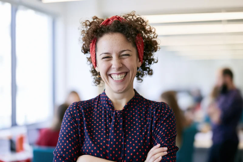 Woman laughing with arms crossed in modern office setting