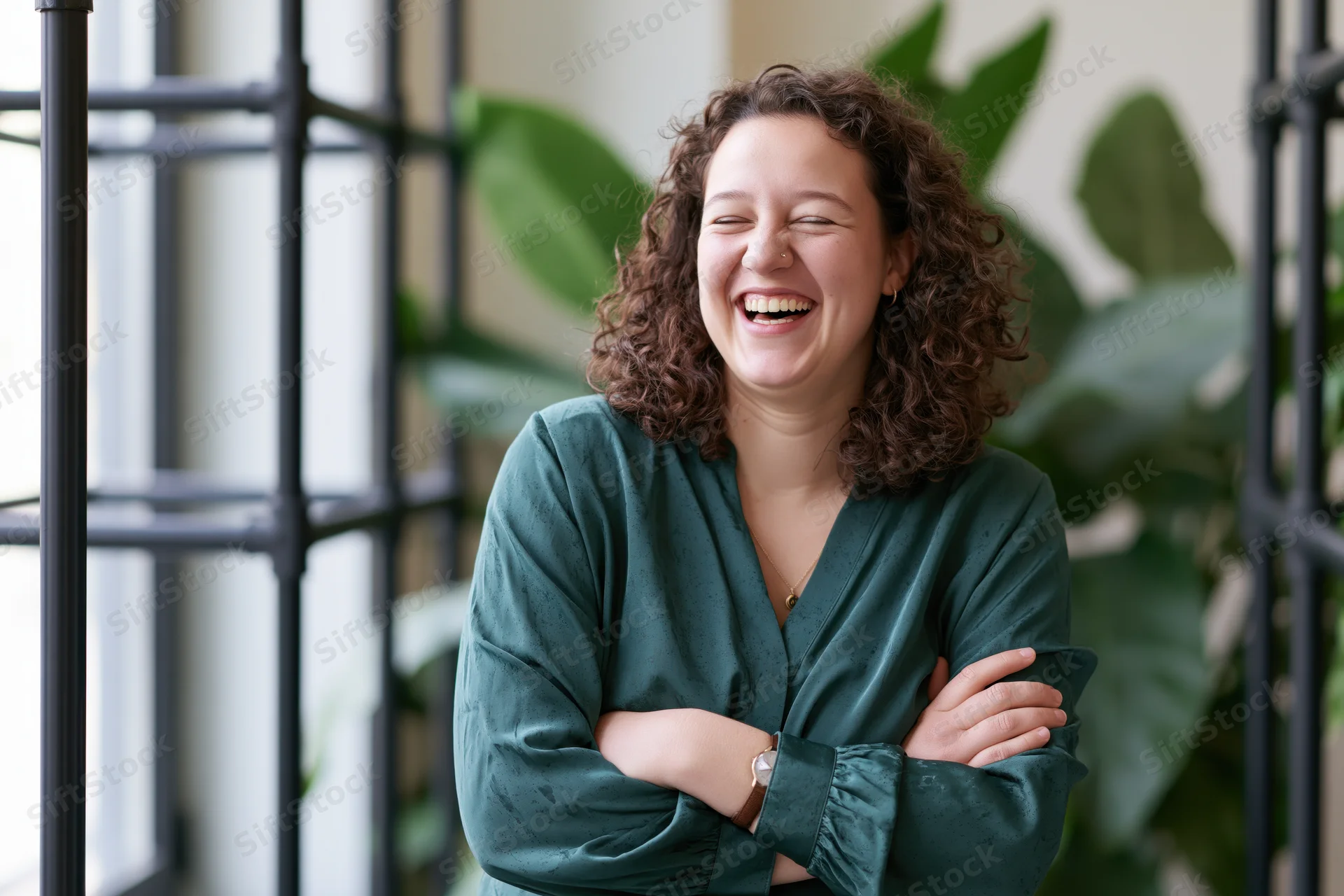 Woman laughing with arms crossed in an office setting near a window with plants in the background