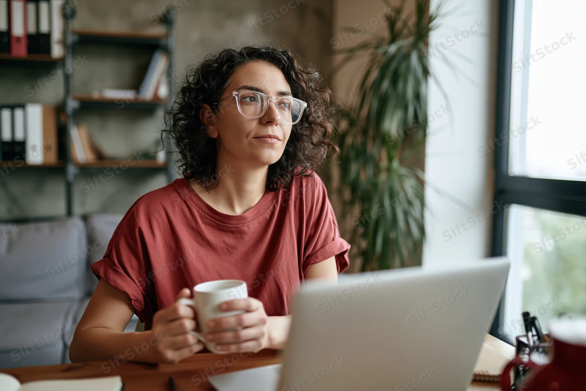 Woman holding coffee mug while working on laptop at home office desk