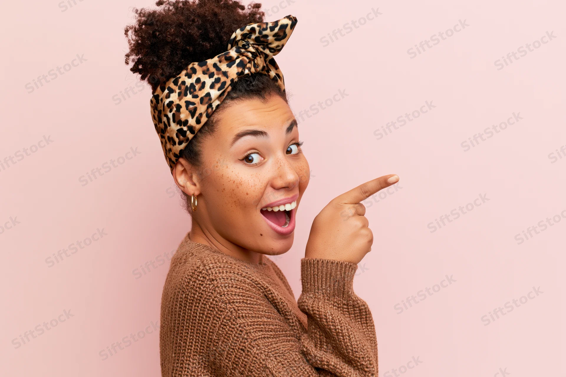 Young woman with curly hair in a bun wearing leopard headband pointing to the side with a happy expression against pink background
