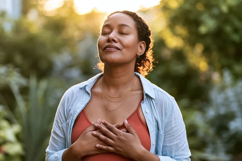 Young black woman with eyes closed and hands on chest in a garden at golden hour