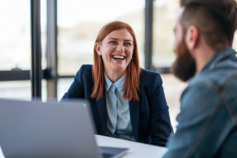 Woman laughing during conversation with colleague at office desk