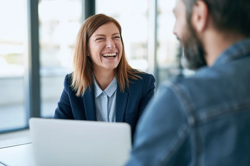 Woman laughing during conversation with colleague at office desk