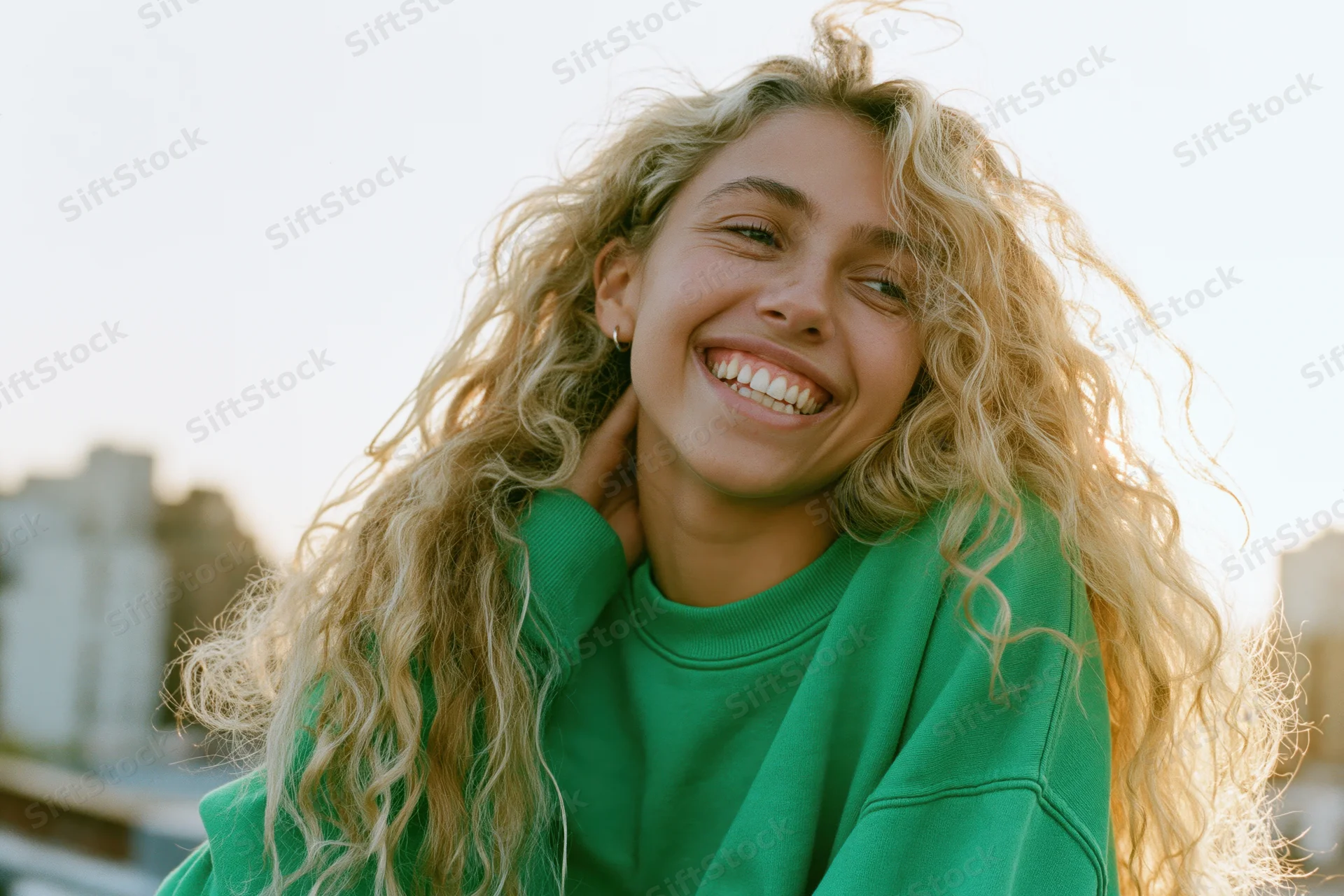 Young woman laughing with curly blonde hair outdoors in city light wearing green sweatshirt