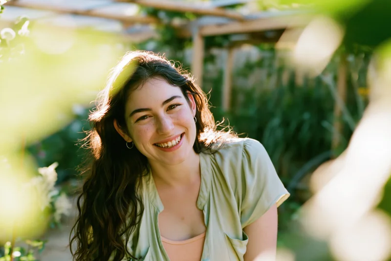Young woman smiling warmly in a sunlit garden with green foliage around her