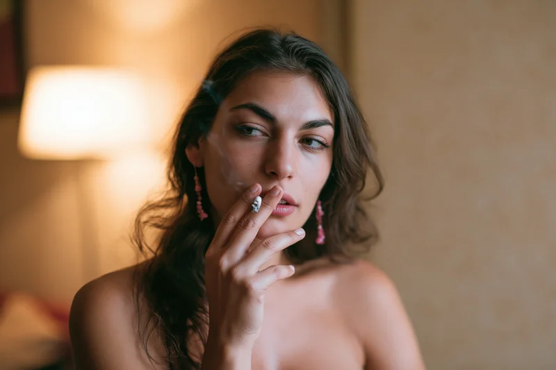 Woman smoking a cigarette indoors with warm lamp light in a close-up portrait