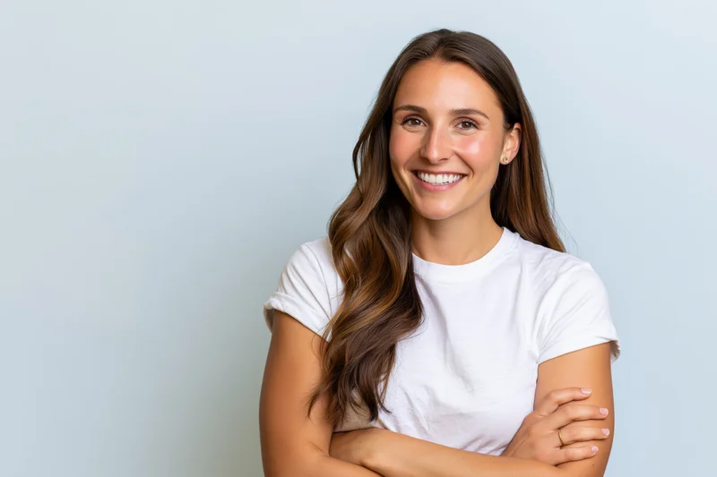 Young woman smiling with arms crossed against light blue background