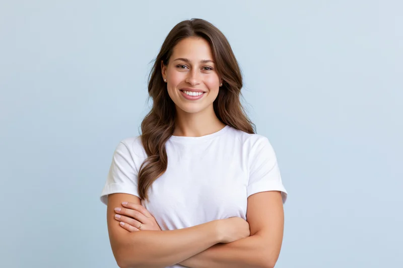 Young woman smiling with arms crossed in white tshirt against light blue background