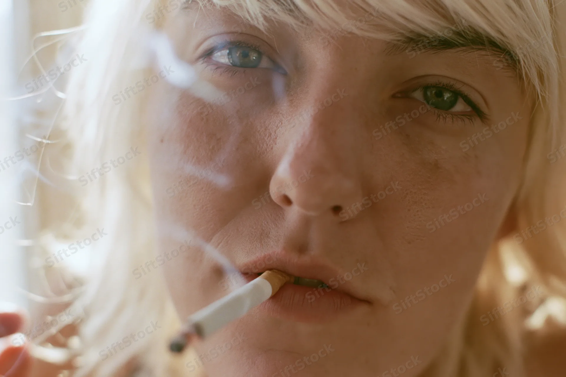 Closeup of a woman with platinum blonde hair smoking a cigarette indoors
