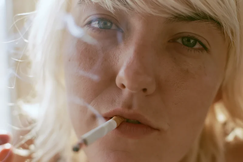 Closeup of a woman with platinum blonde hair smoking a cigarette indoors