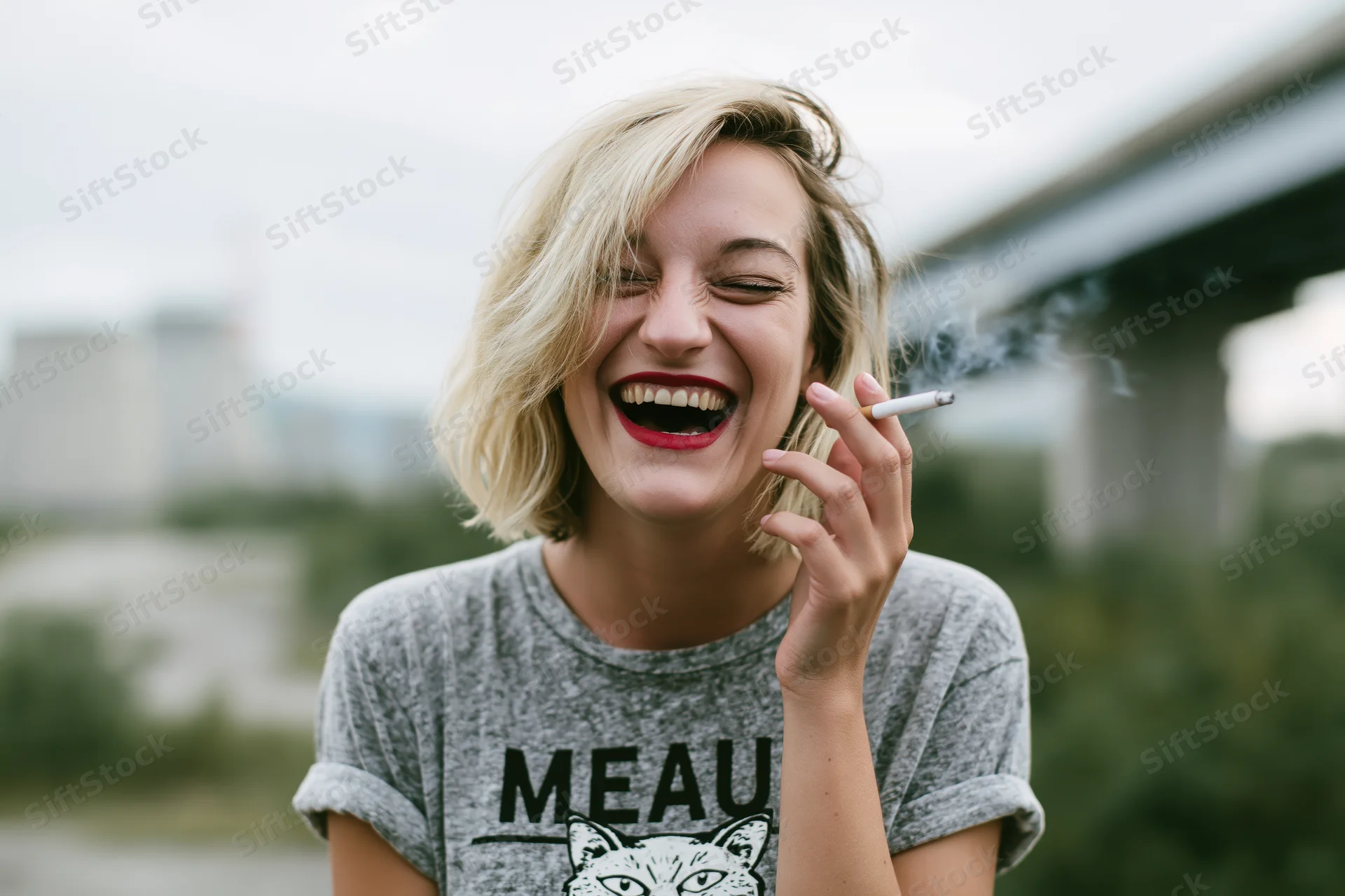 Woman laughing while smoking a cigarette outdoors near a bridge