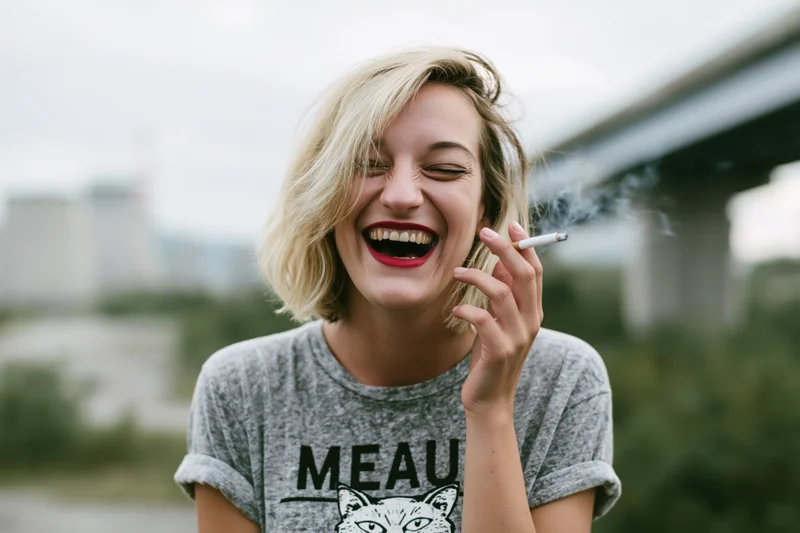 Woman laughing while smoking a cigarette outdoors near a bridge