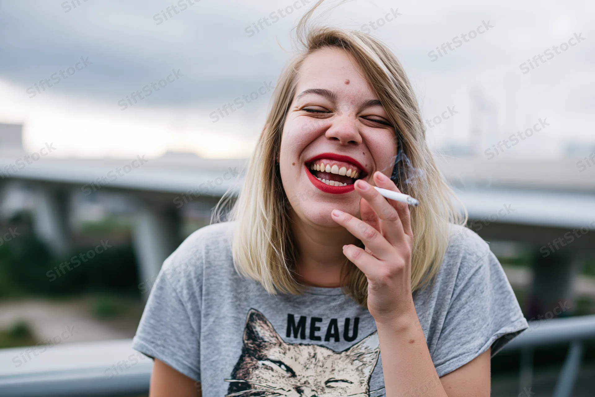 Young woman laughing while smoking a cigarette outdoors on a balcony