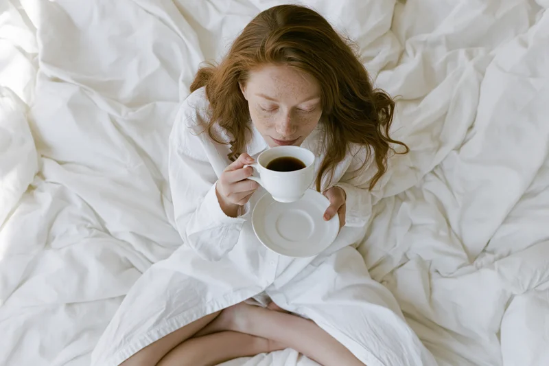 Woman sitting cross-legged in bed holding a cup of coffee in the morning