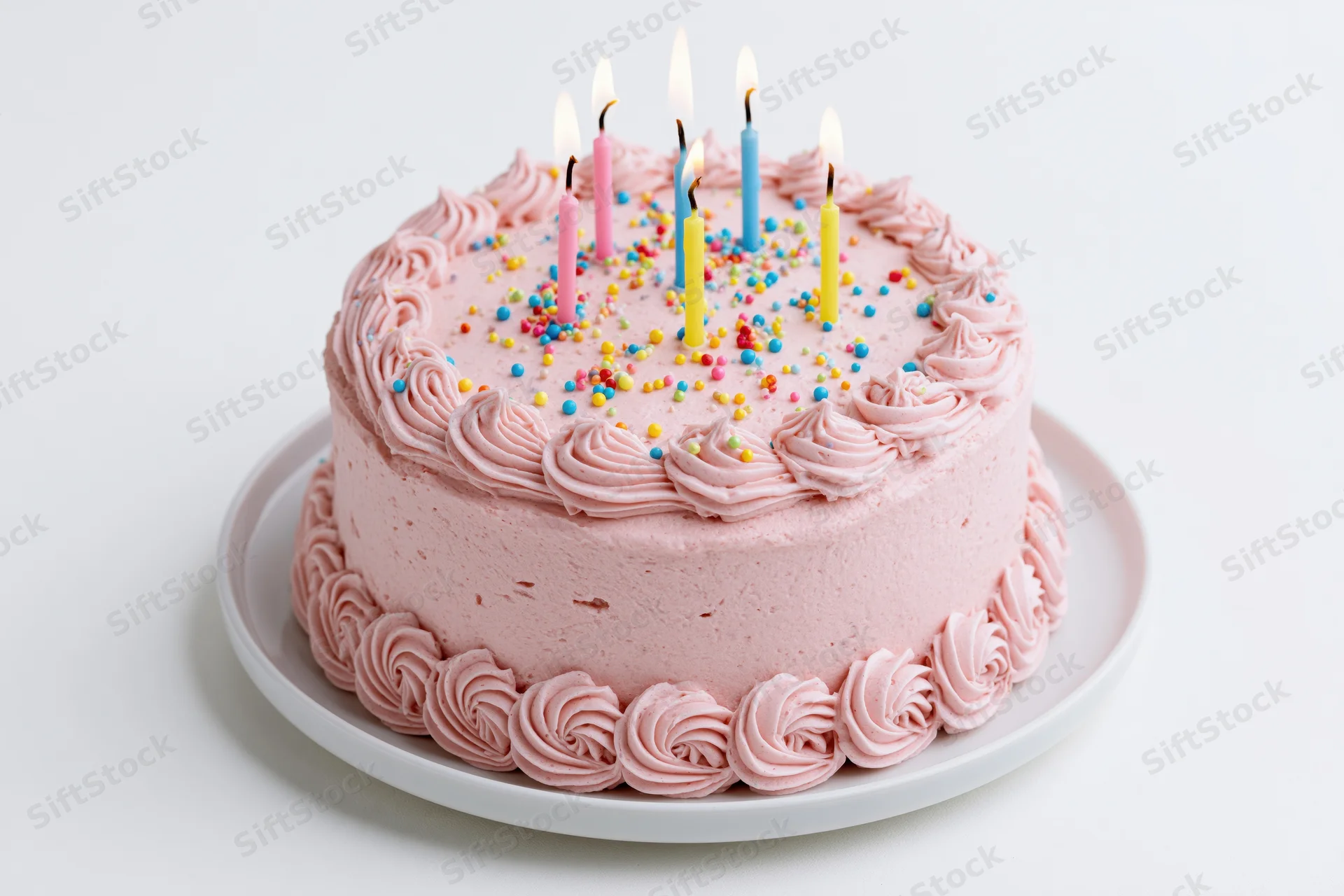Round birthday cake with pink frosting and lit candles on white plate
