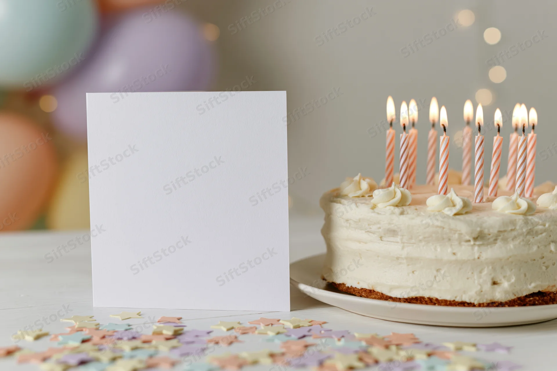 Blank white greeting card standing beside a birthday cake with lit candles on a table scattered with confetti and balloons in the background