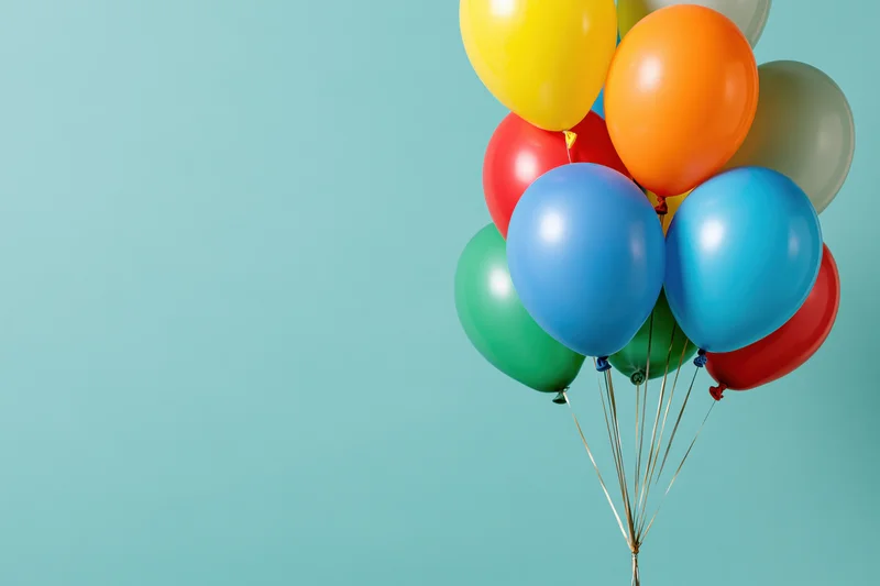 Colorful latex balloons clustered together on a light blue background with copyspace on the left