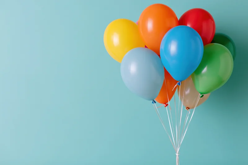 Colorful latex balloons clustered together against a light blue background with copyspace