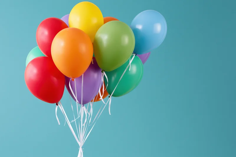 A cluster of colorful latex balloons tied together with white string against a teal background