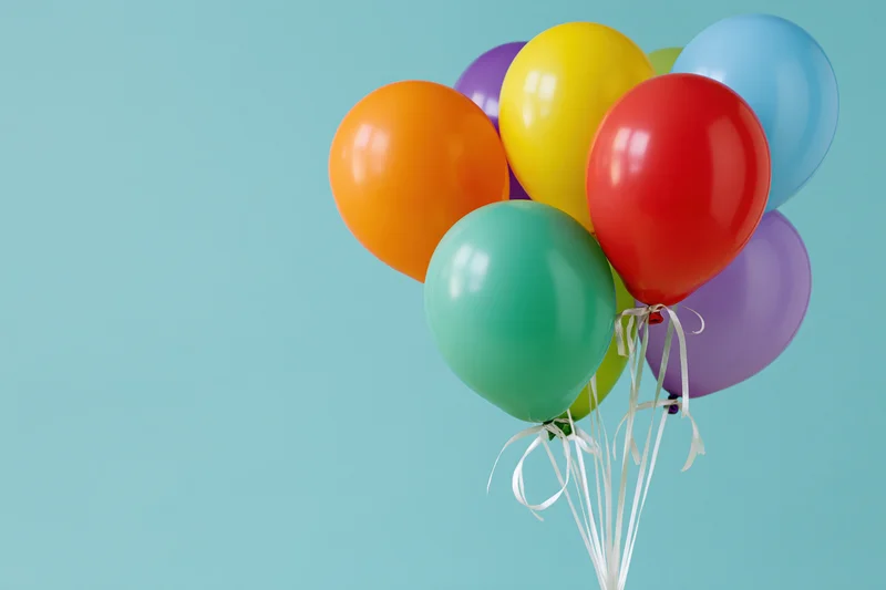Colorful latex balloons tied together with white ribbons against a light blue background