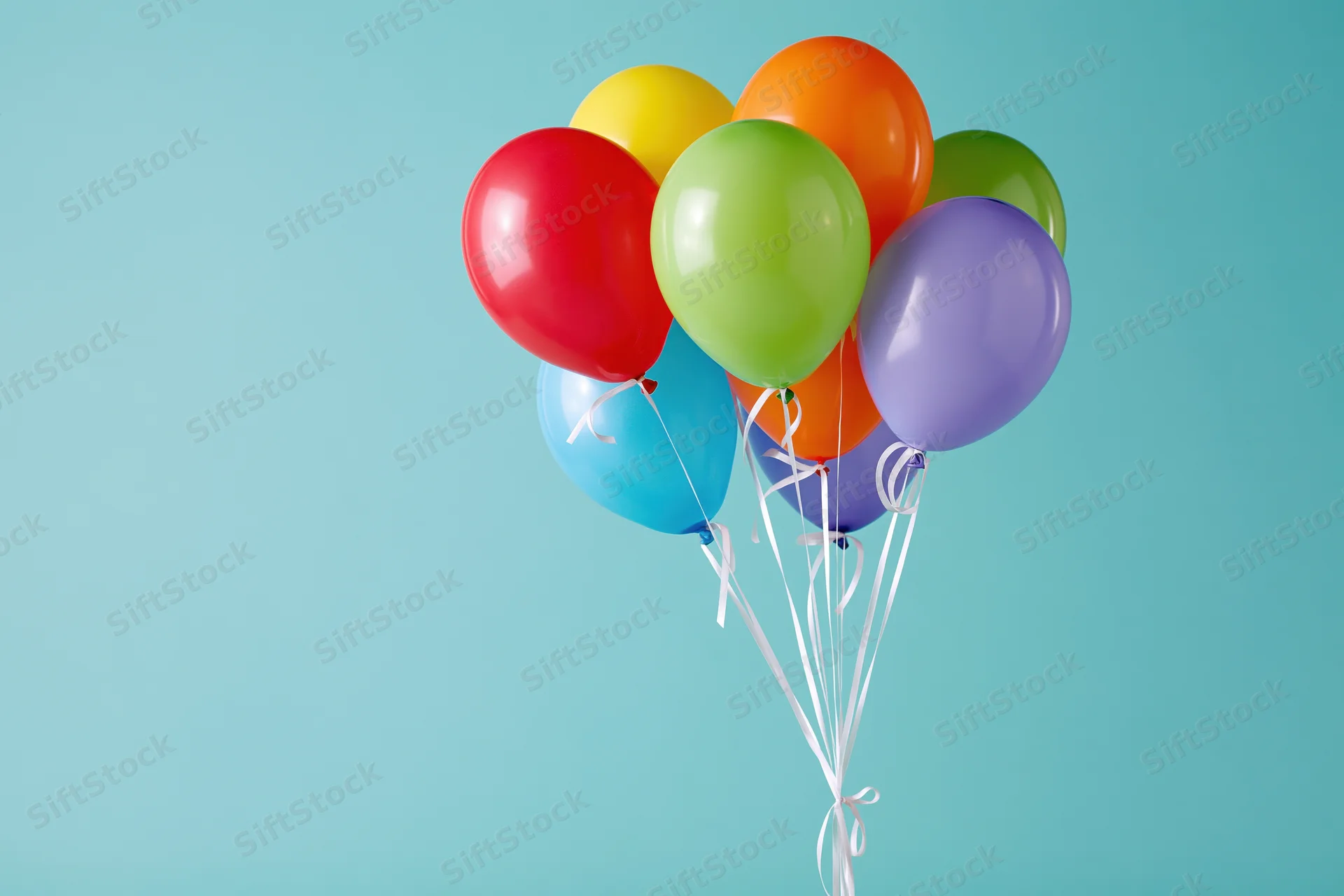 Colorful latex balloons tied together with white ribbons floating against a light blue background