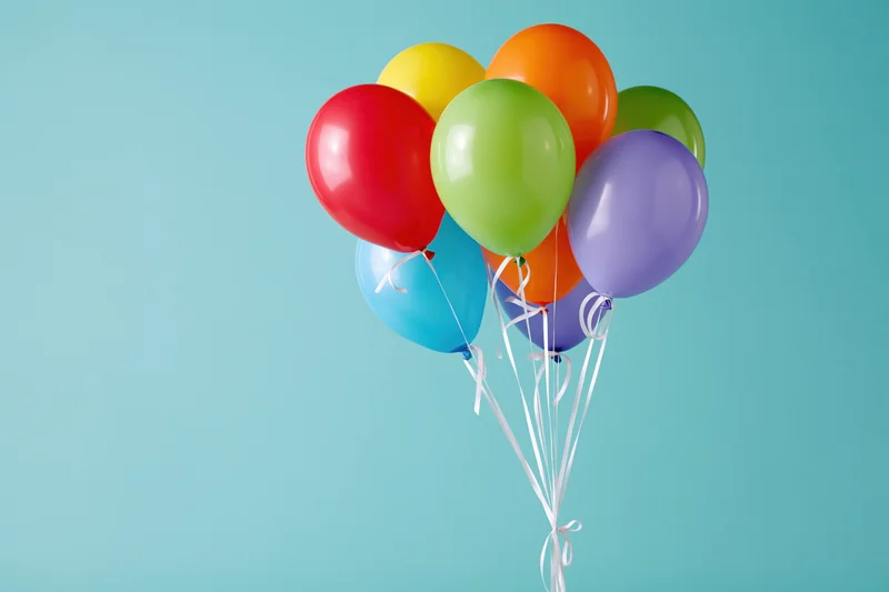 Colorful latex balloons tied together with white ribbons floating against a light blue background