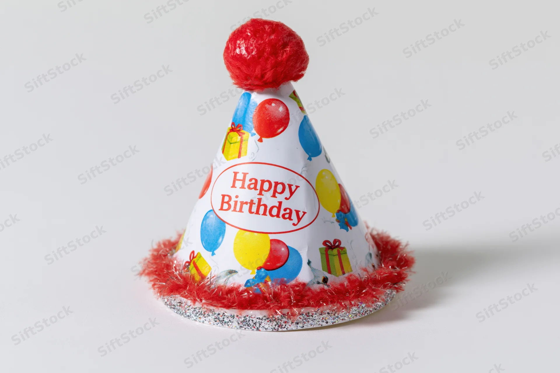 Colorful paper birthday party hat with red pompon and fringe sitting upright on white background
