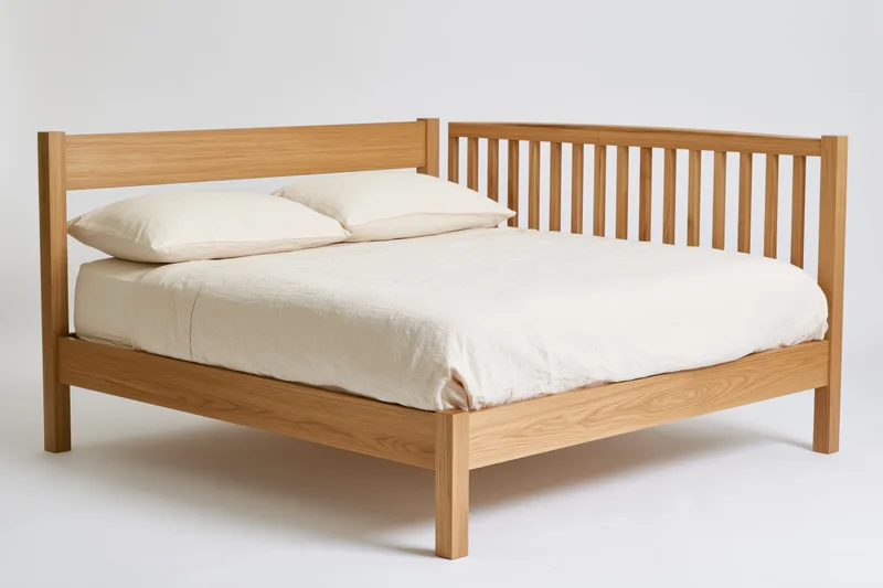 Double bed with solid oak wooden frame and white bedding on plain background