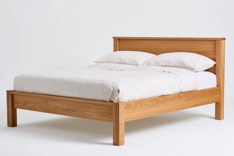 Double bed with solid oak wooden frame and white bedding on plain background