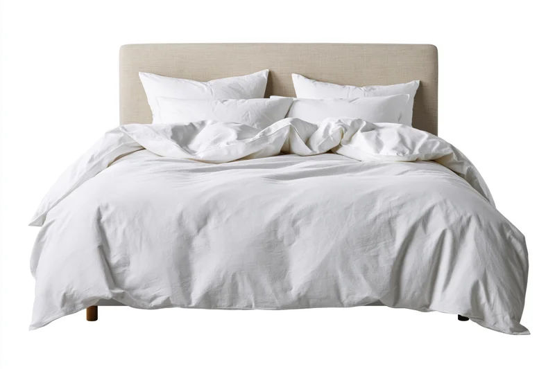 Double bed with white cotton bedding and rumpled duvet against white background