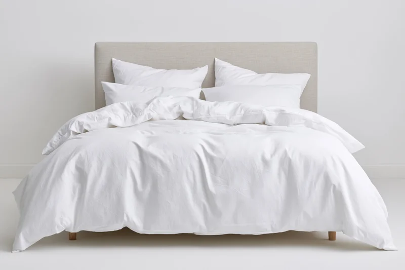 Double bed with white cotton bedding and rumpled duvet in minimalist bedroom