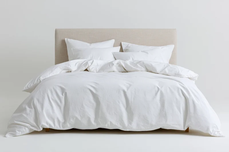 Double bed with white cotton bedding and rumpled duvet against plain white background