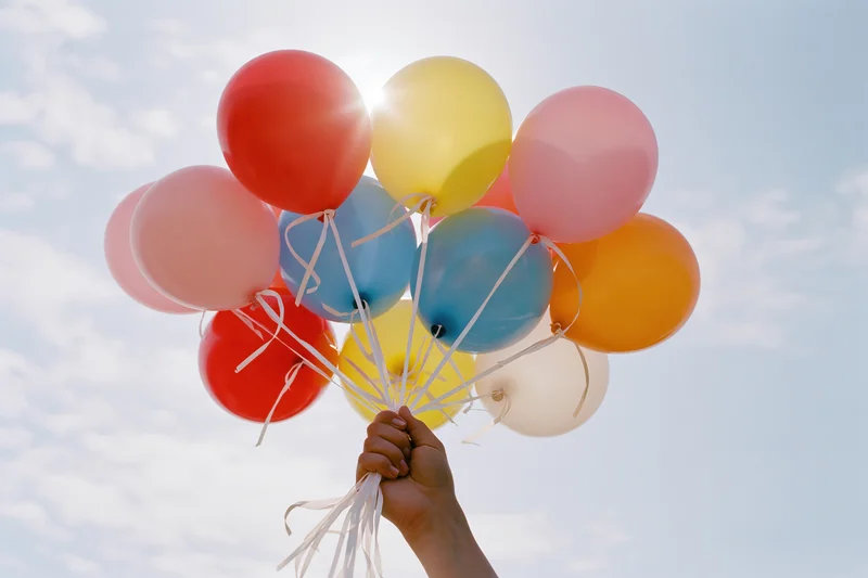 Hand holding a bunch of multicolored latex balloons against a bright sky