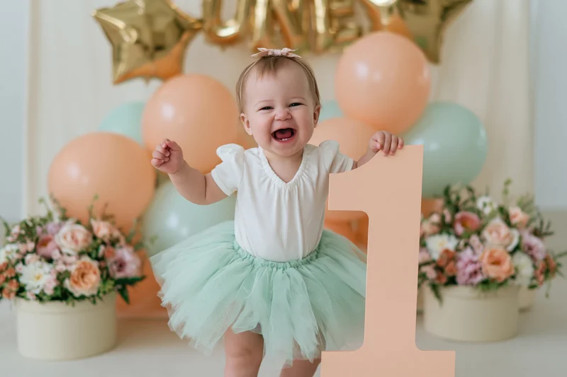 Laughing baby girl holding large number one at first birthday party