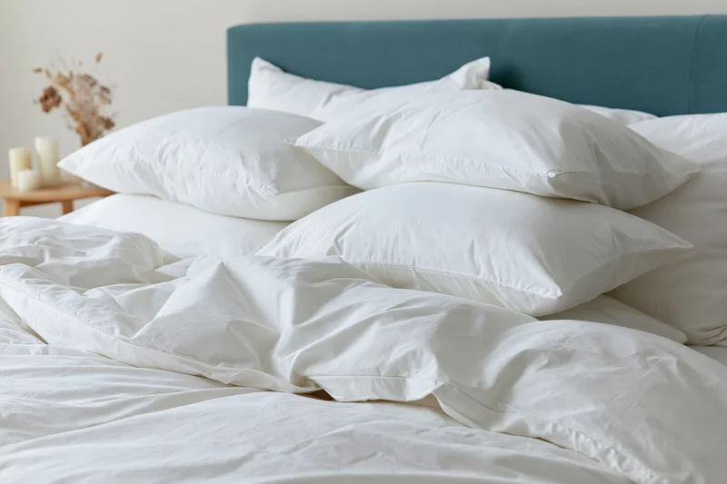 Neatly arranged bed with stacked white pillows and teal headboard in a bedroom