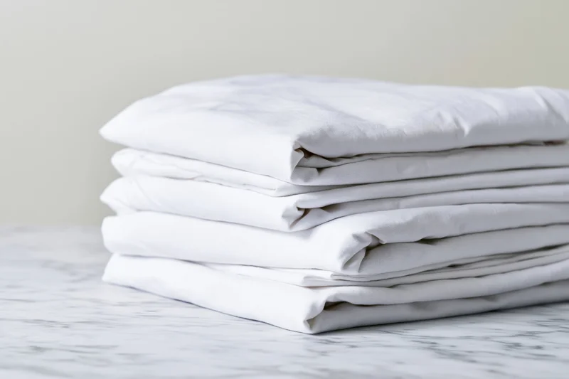Stack of neatly folded white cotton bed sheets on a marble surface