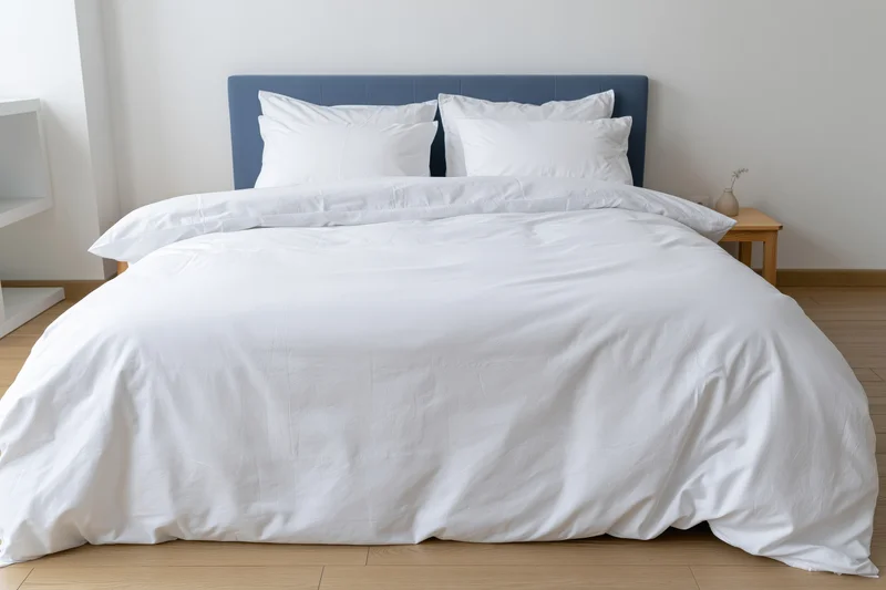 Neatly made bed with white cotton duvet and multiple white pillows against blue headboard in minimalist bedroom