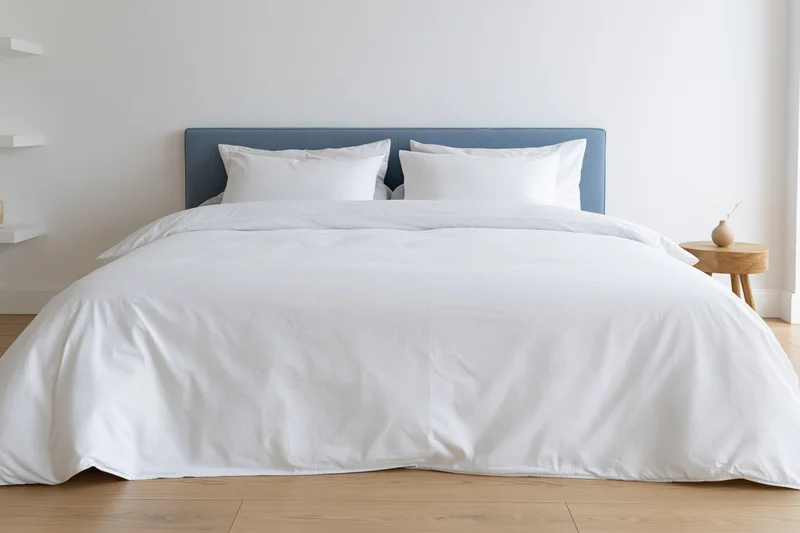 Neatly made bed with white duvet and pillows in a minimalist bedroom