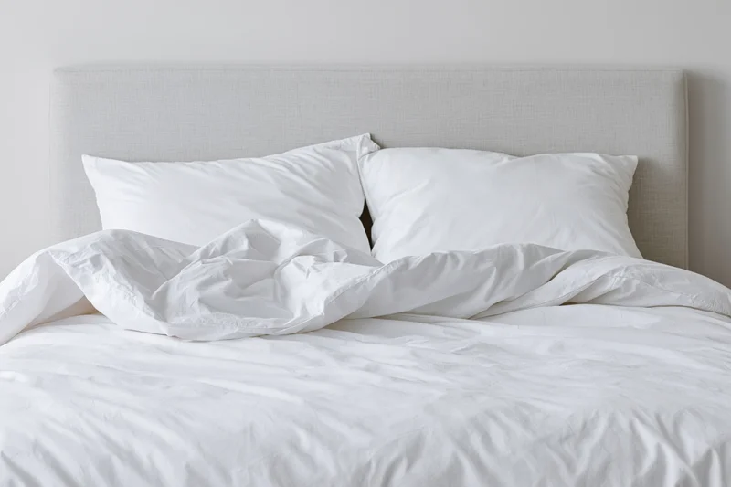 Unmade double bed with white pillows and rumpled bedding in a minimalist bedroom