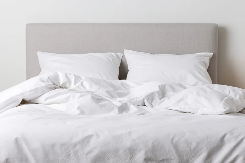 Unmade double bed with white bedding and gray headboard in a minimalist bedroom