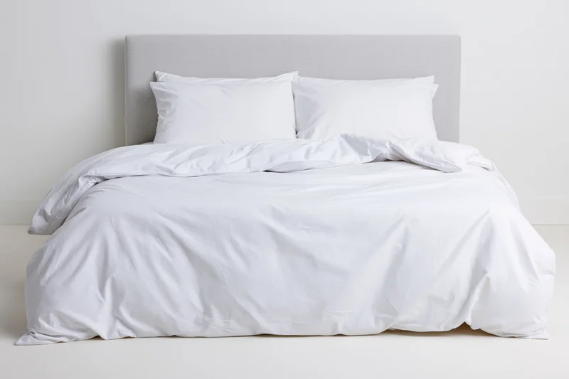 White bedding on a double bed with gray headboard in a minimalist bedroom