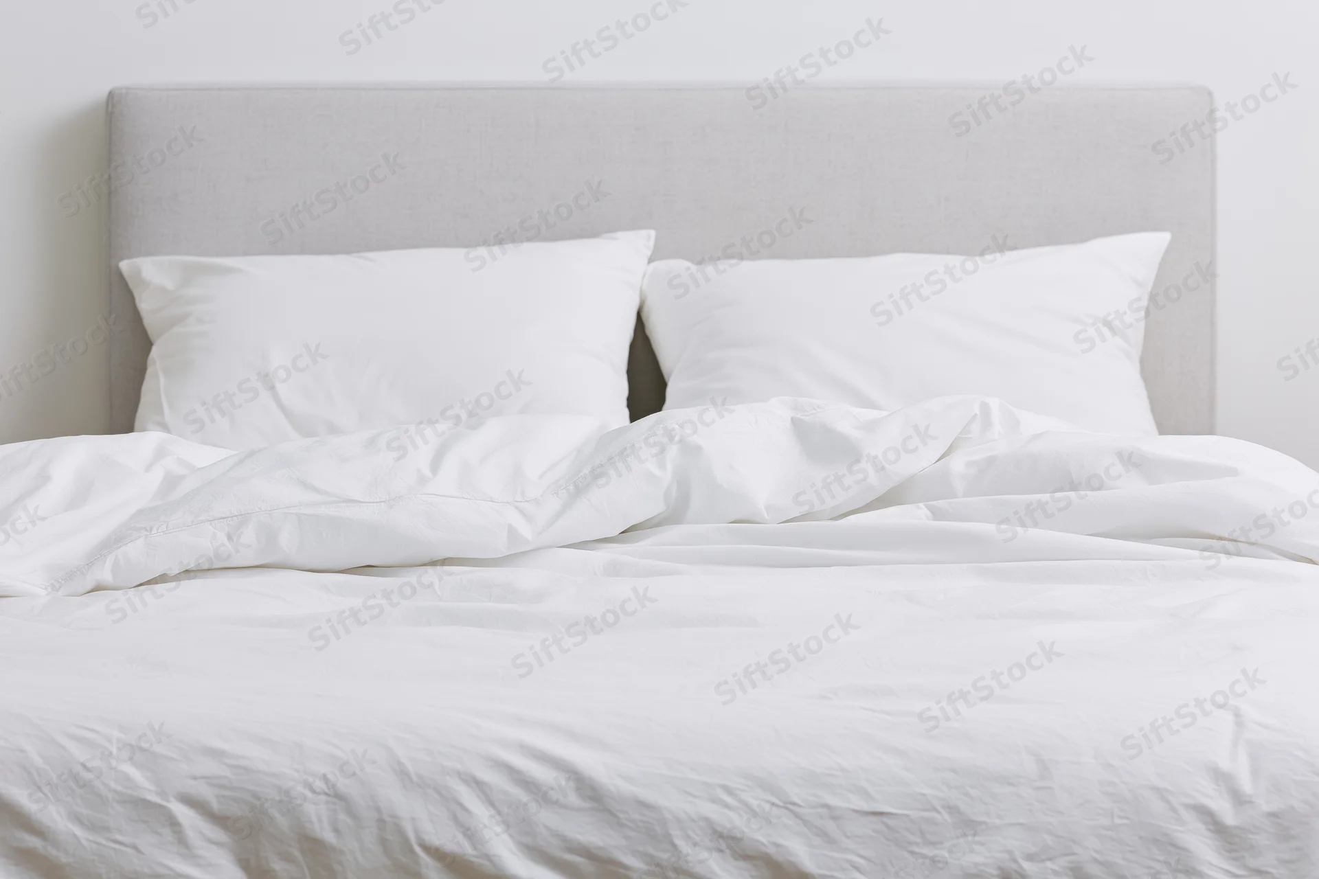 Unmade double bed with white bedding and gray headboard in a minimalist bedroom