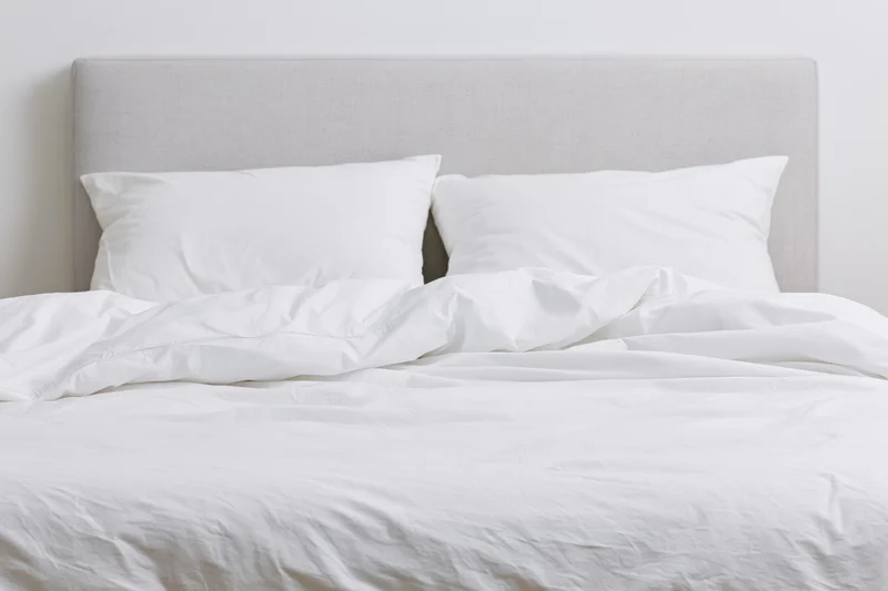 Unmade double bed with white bedding and gray headboard in a minimalist bedroom