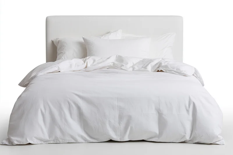 White bed with duvet and pillows on plain background