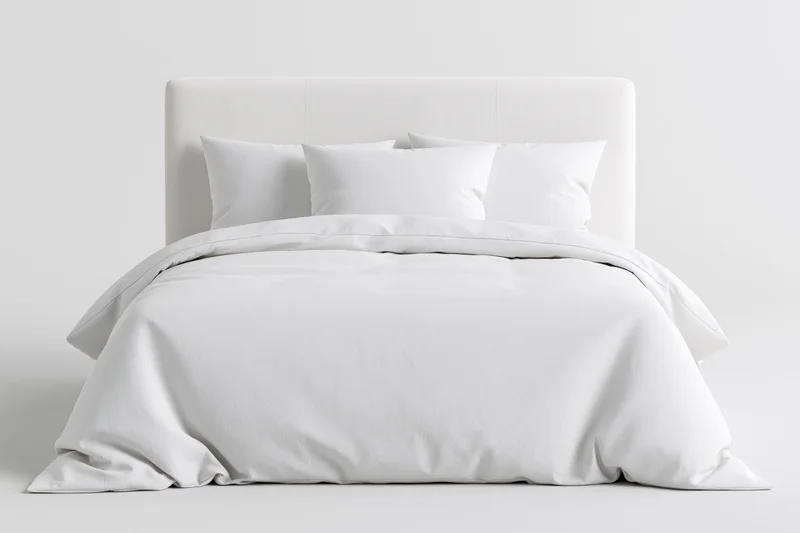 White double bed with cotton duvet and three pillows against plain background